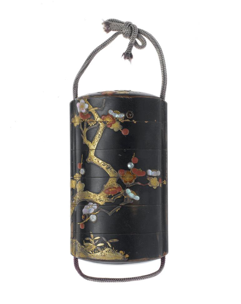 A cylindrical case made of dark lacquered wood with gold floral details. A cord loops around the sides and ties at the top of the case.