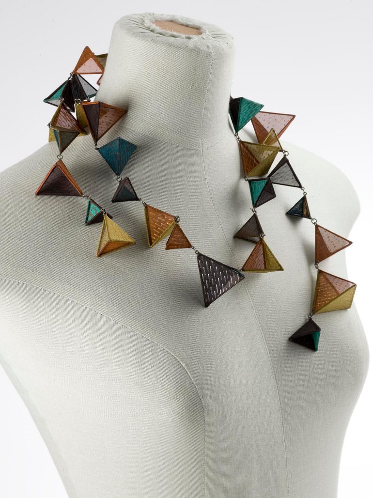 A mannequin bust wearing a necklace made of orange, brown, and green triangular pieces.