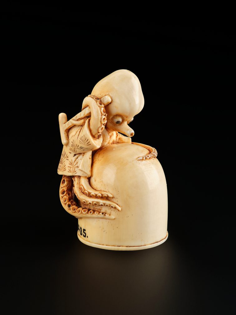 A small carved ivory object of an octopus holding a hammer, wrapped around an inverted jar