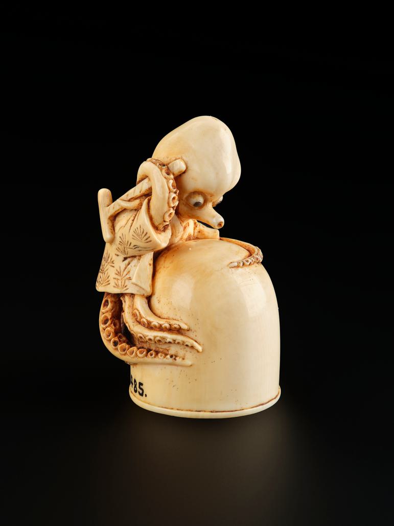 A small carved ivory object of an octopus holding a hammer, wrapped around an inverted jar