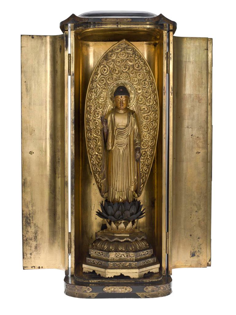 A gold shrine of a buddah statue set against a decorated oval plate.