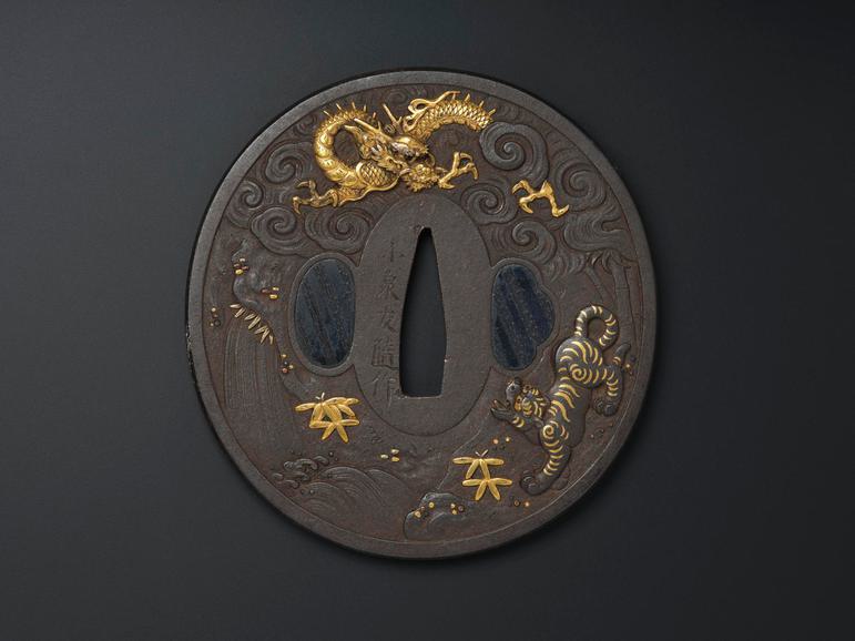 A dark circular object with an oval hole in the middle with decorations on the surface including a gold dragon and tiger