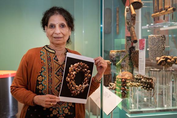 A person stands next to a museum display case, holding a print facsimile of a golden anklet