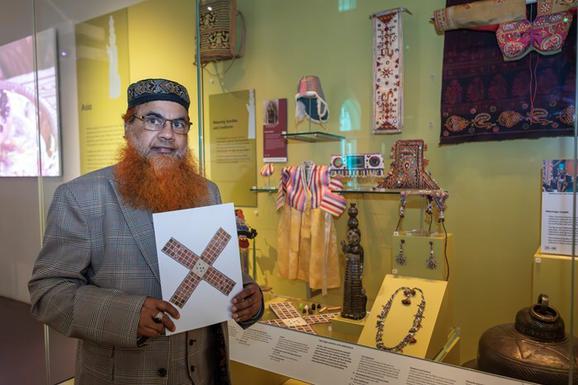A person stands in a gallery, holding a printed facsimile of the chausur board