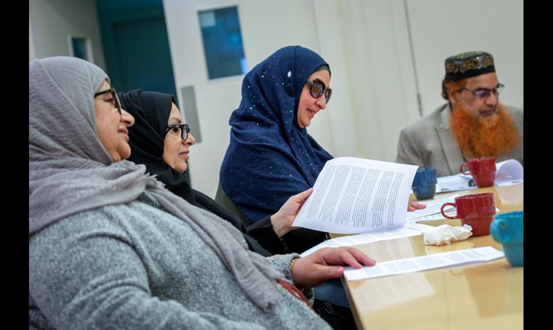 A group of four people sit around a table in discussion.