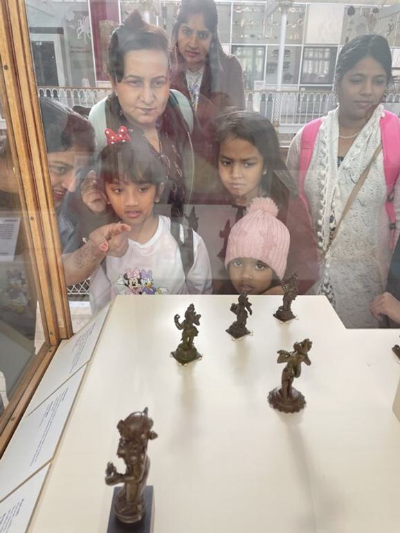 A group of people of mixed ages observe statues in a glass case