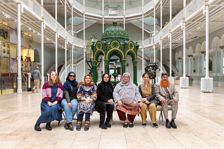 A group of seven people pose for a photo in front of a large green drinking fountain