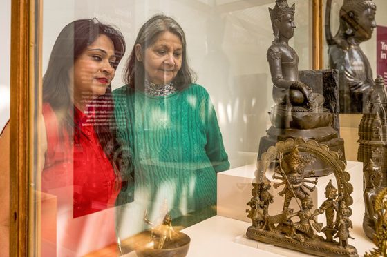 A person wearing red and a person wearing green gaze at a statue in a glass case