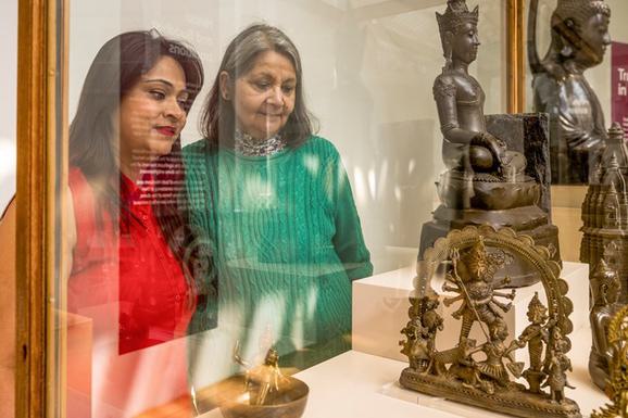A person wearing red and a person wearing green gaze at a statue in a glass case