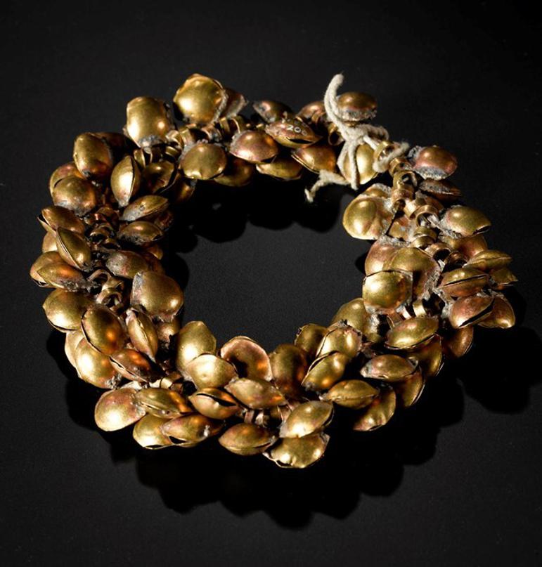 An ornate, golden anklet pictured against a dark black background