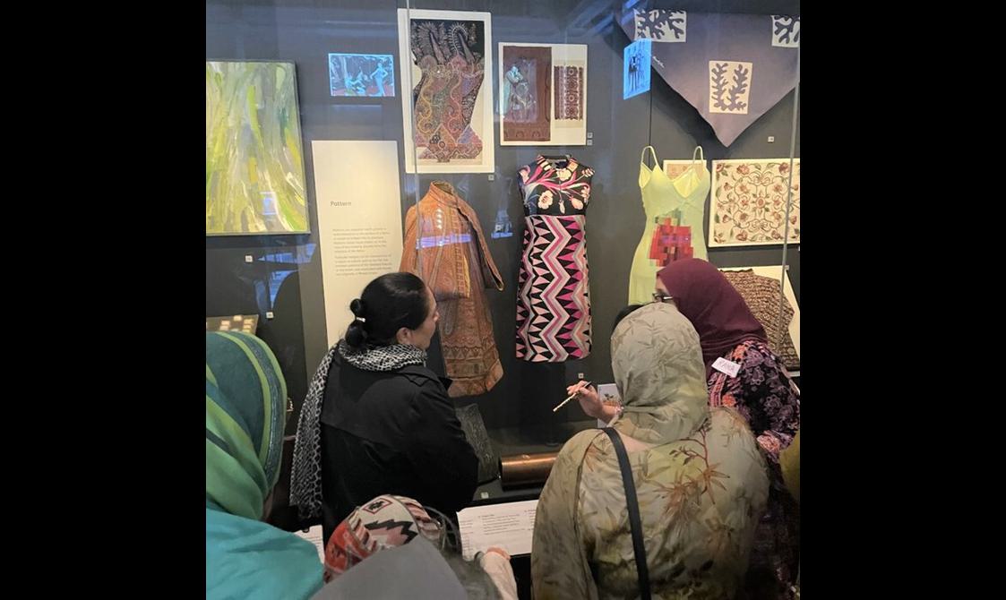 A group of people are looking closely at a piece of decorated fabric hung in a display