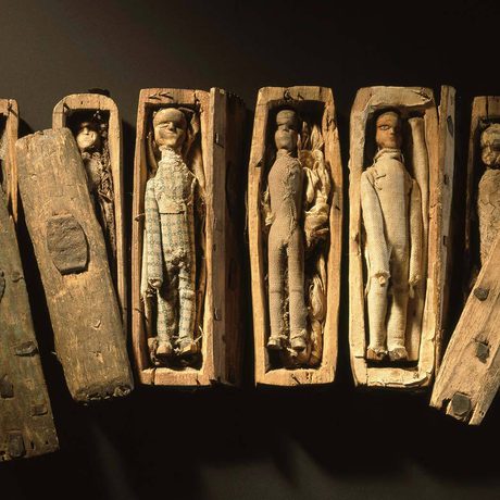 A row of miniature coffins with dolls inside them.