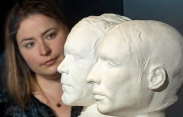 A curator looking side on at two life masks of William Burke and William Hare.