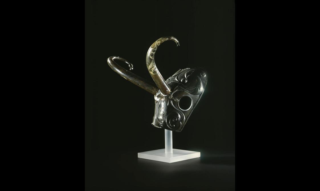 A bronze mask with circular eye sockets and curved horns.