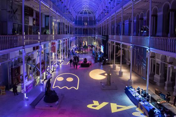 The Grand Gallery set up for an evening event lit with pink and purple lighting, with projections of Pacman characters on the floor.