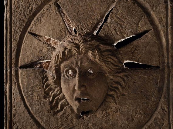 A Roman stone altar with the face of the Roman god Sol carved into it. Rays of light pass through slits around the head of Sol.