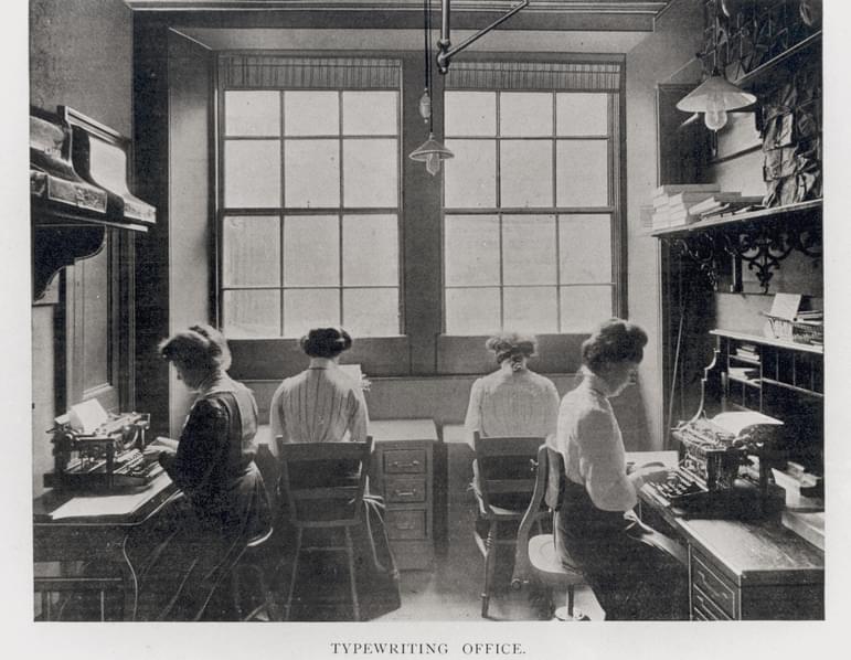A black and white photograph of four typists working at office desks.