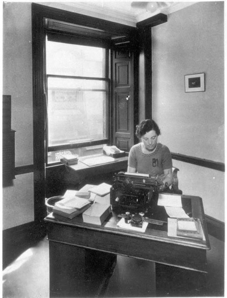 A black and white photograph of a typist working at a desk.