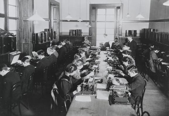 A black and white photograph of four rows of people using typewriters.