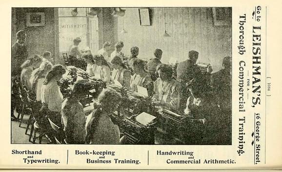 A black and white photograph of two rows of people using typewriters.