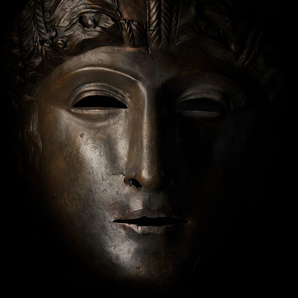 Dramatic bronze face mask of a Roman on a black background