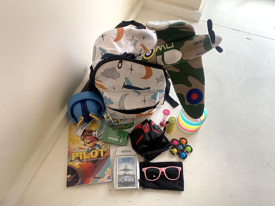 An open patterned white backpack surrounded by a variety of sensory toys and objects.