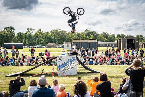 A BMX rider in the air mid flip while a crowd watch