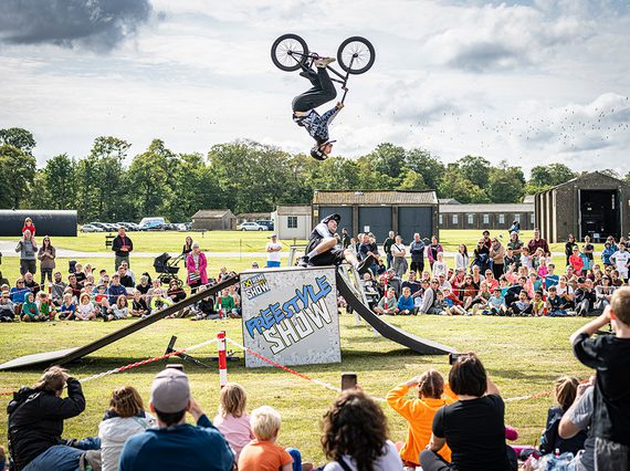 A BMX rider in the air mid flip while a crowd watch