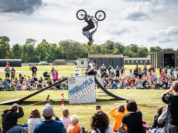 A BMX rider in the air mid flip while a crowd watch