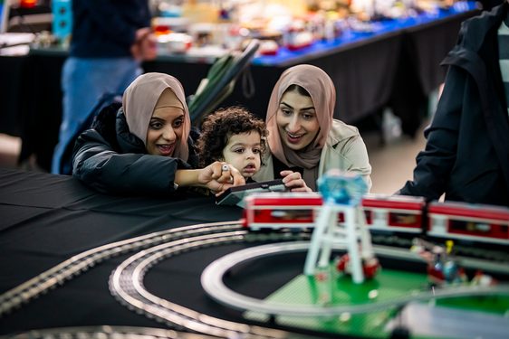 Adults with young child looking at a model LEGO train set