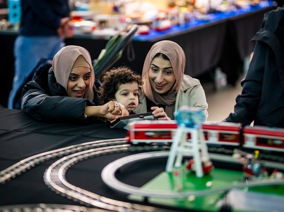 Adults with young child looking at a model LEGO train set