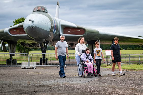 A family of two adults and three children, one using a wheelchair, in front of the Vulcan aircraft outdoors at the National Museum of Flight.