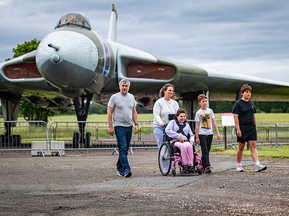 A family of two adults and three children, one using a wheelchair, in front of the Vulcan aircraft outdoors at the National Museum of Flight.