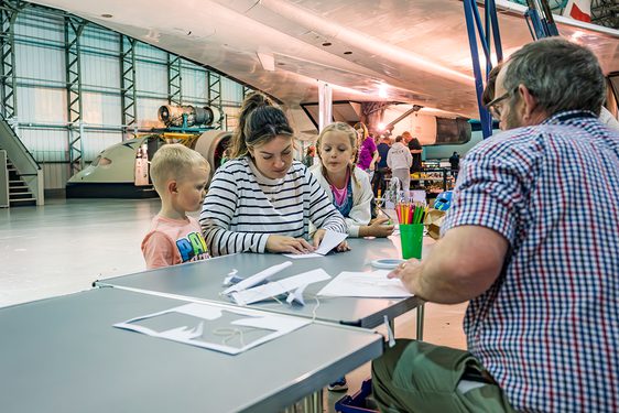 A family sit at a table, making a glider out of paper