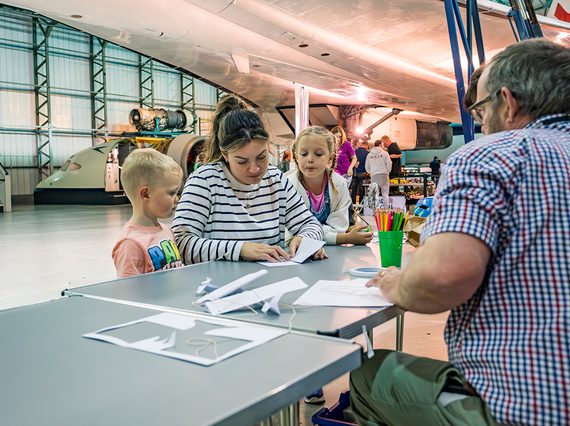 A family sit at a table, making a glider out of paper
