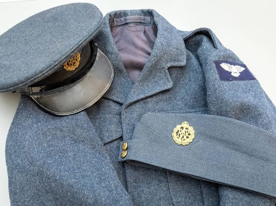 A blue wool uniform coat with a patch showing white wings on the left arm. A wool cap with a black brim and a gold RAF insignia sits on top of the coat.