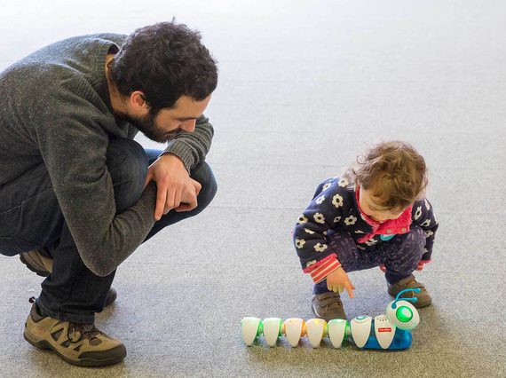 An adult and child crouch over a colourful caterpillar robot toy with big green lights for eyes.