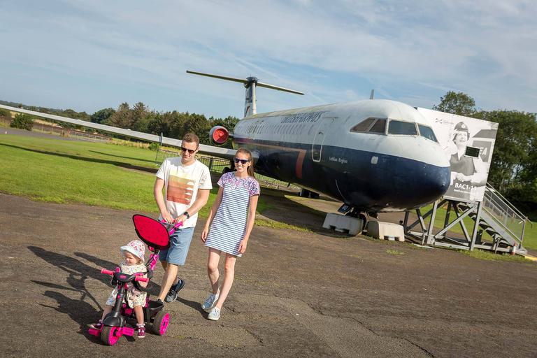 Parents pushing their child in a pink pushchair next to an aircraft at the East Fortune airfield.