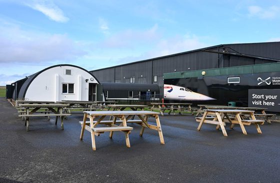 A group of wooden picnic benches outside the Aviator Café at the National Musuem of Flight.
