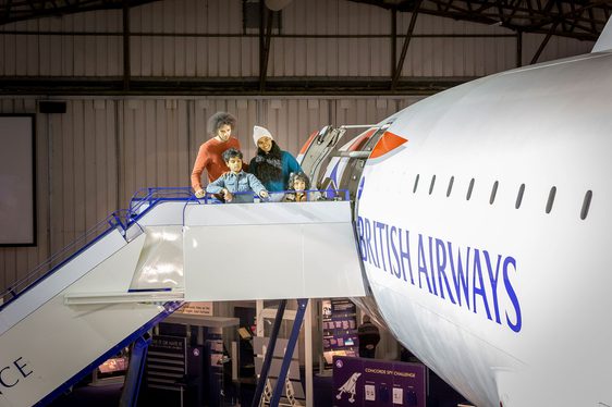 A family of four standing on boarding steps outside the door of a Concorde aeroplane.