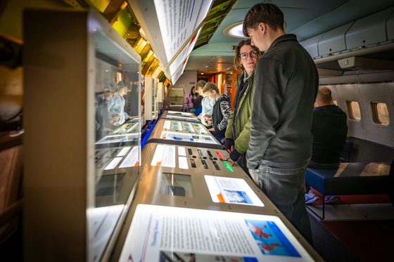 Adults and children interacting with hands-on displays in an aeroplane cabin.