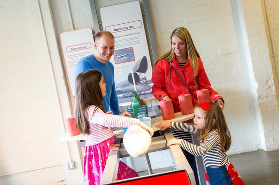 A family of four playing with a balancing game in the Fantastic Flight gallery.