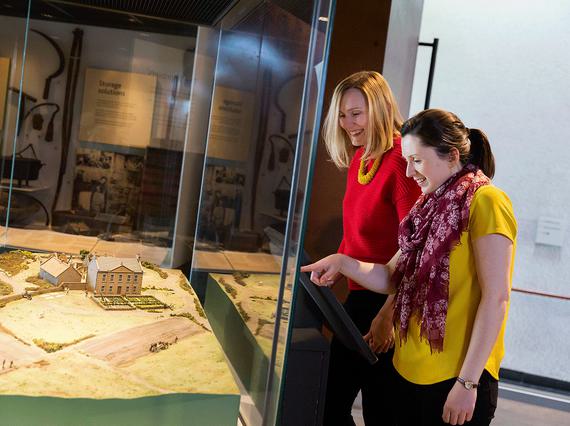 Two visitors looking at a model of a farm in a museum display case.