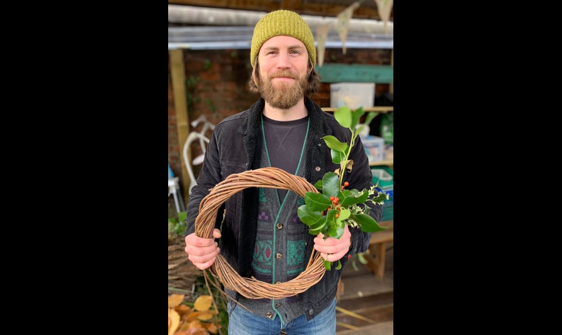 Artist and forager Max Johnson standing smiling holding a festive willow wreath