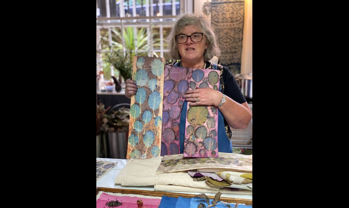 A woman holding up examples of colourful botanical prints in an art studio.