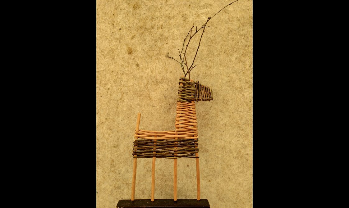 A willow reindeer decoration made out of willow against a yellow wall.