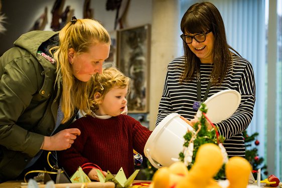 A mother and child take part in a festive crafts session with a member of museum staff