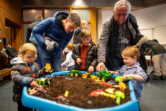 An intergenerational family are playing in a soil pit filled with soil and toy bugs.