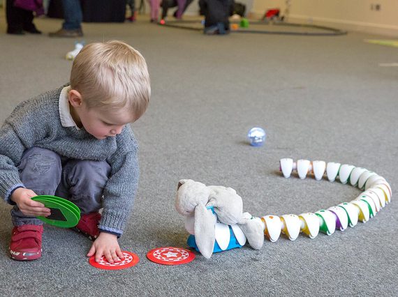 A child kneeling down placing red place cards on the floor for a toy snake to follow.