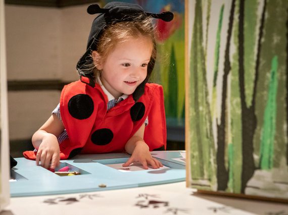 A small child dressed as a ladybird leans over a table with craft supplies on it.
